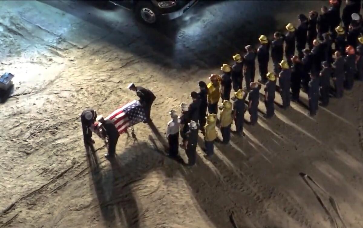 Overhead view of firefighters lined up watching a flag-draped gurney