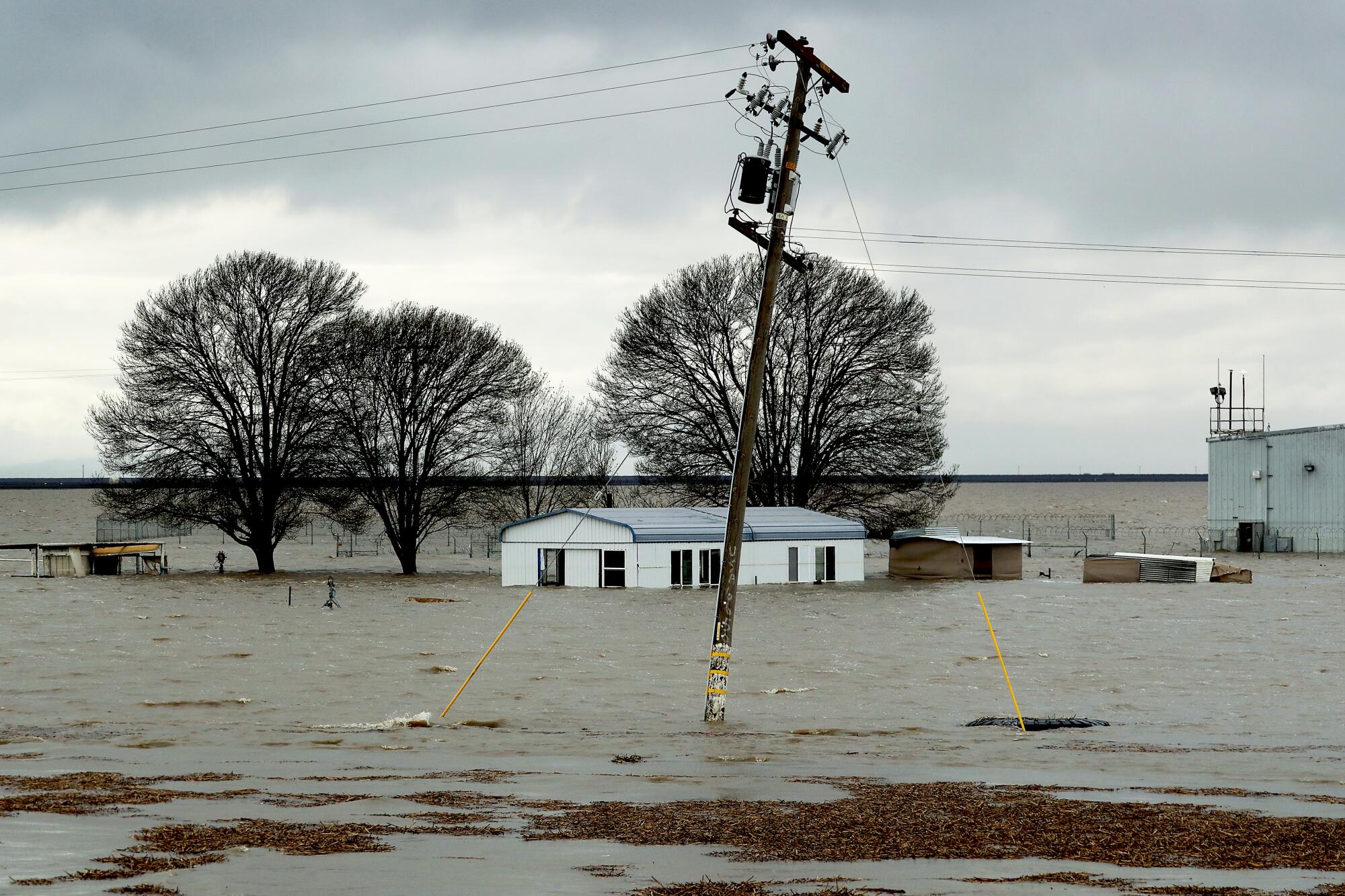 Floodwaters surround a house structure. A telephone pole leans from the water at the center. 