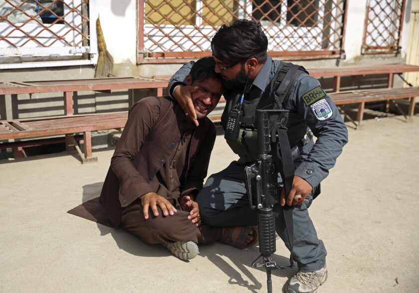 FILE - In this May 12, 2020 file photo, an Afghan policeman comforts a man after an attack on a maternity hospital that killed 24 people, in the Afghan capital Kabul. Afghanistan is supposed to be moving toward peace. But Kabul's residents fear the frequent bombings in the past months, large-scale attacks, kidnappings for ransom, armed men in broad daylight robbing stores, people in parks and cars stuck in traffic, are a sign it is instead entering yet another phase in decades of war. (AP Photo/Rahmat Gul, File)