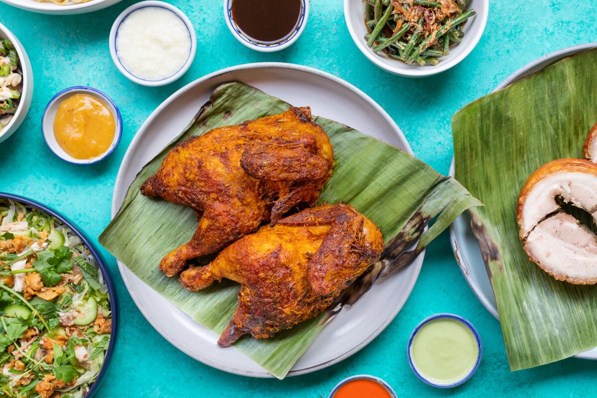 Pieces of cooked chicken plated on a grassy sheet, surrounded by small cups of sauces.