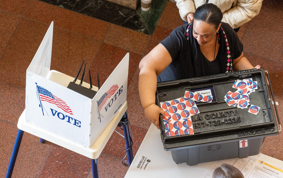 A woman moves a ballot box with stickers on top.