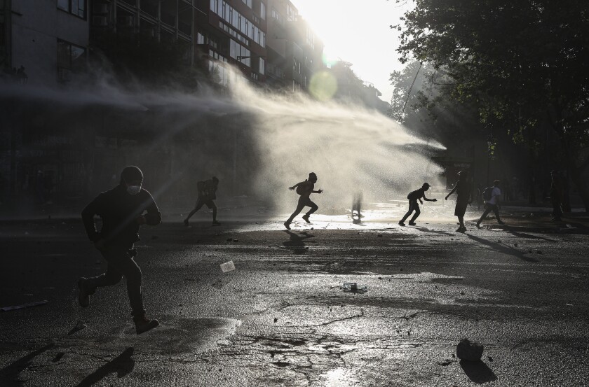 Anti-government protesters run amid the spray of a police water cannon during demonstrations against economic inequality in Santiago, Chile, Wednesday, Oct. 30, 2019. Chilean President Sebastian Pinera cancelled two major international summits after nearly two weeks of nationwide protests that have left at least 20 dead and damaged businesses and infrastructure around the country. (AP Photo/Esteban Felix)