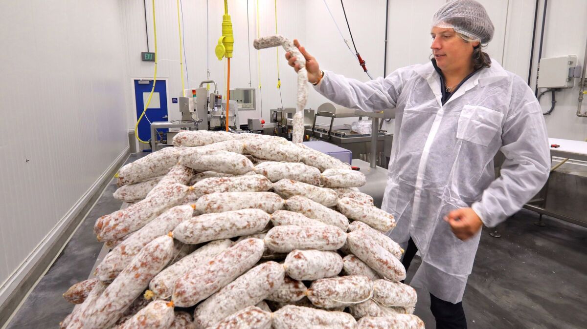 Oliviero Colmignoli hand-tests the firmness of a stack of salami being prepared for packaging at his Olli Salumeria factory in Oceanside.
