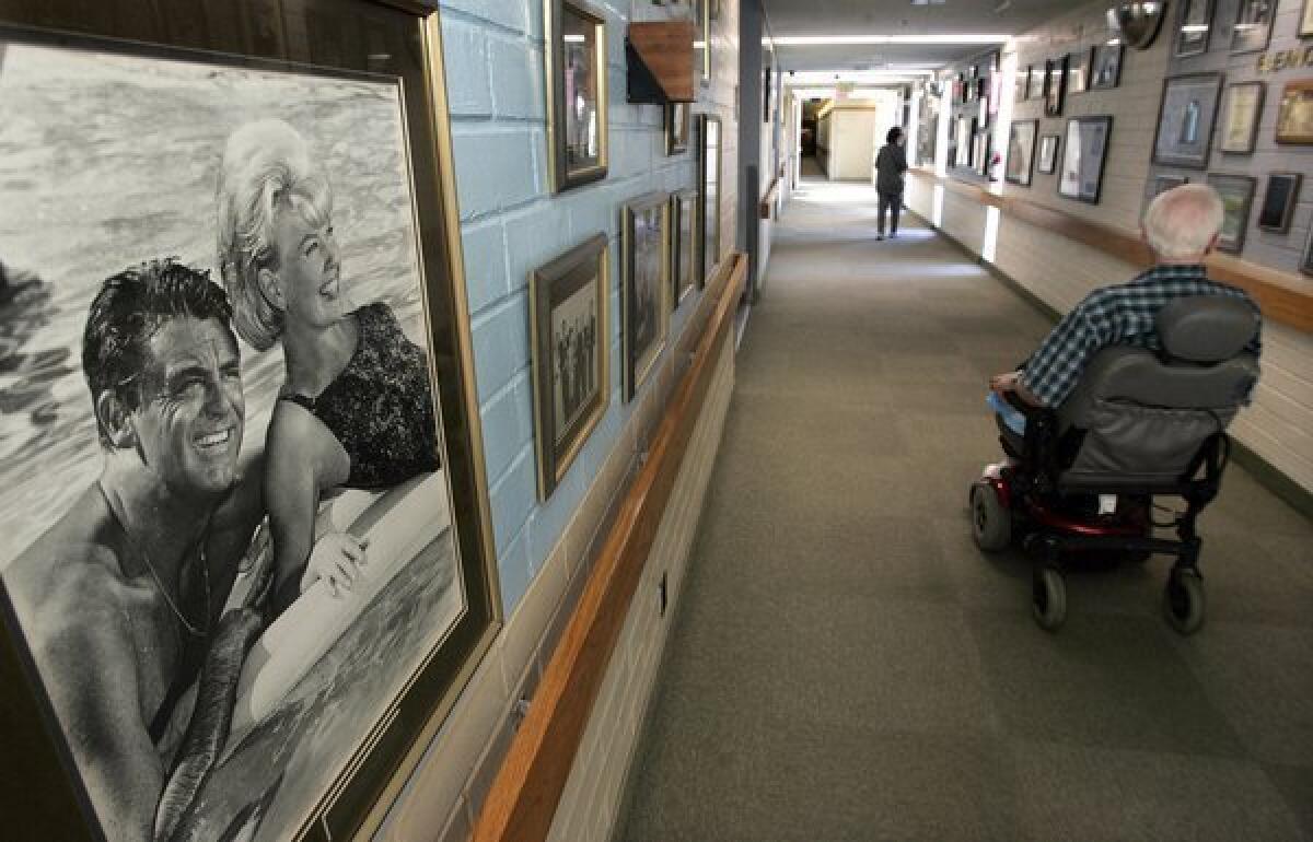 Hal Alexander, 87, a former TV stage manager and associate director, operates his motorized wheelchair past a photograph of actors Cary Grant and Doris Day, in a hallway at the Motion Picture & Television Fund nursing home and hospital in Woodland Hills.