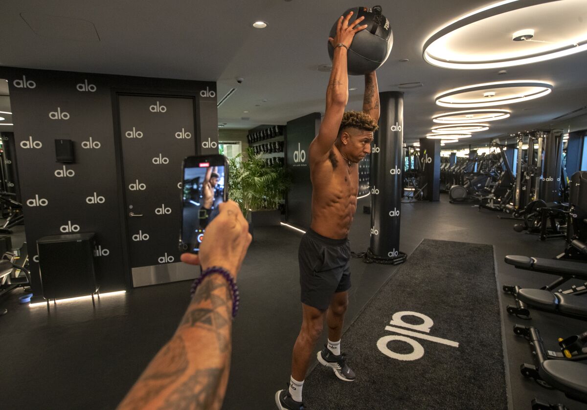 Man holding a cell phone while recording another man working out in a gym