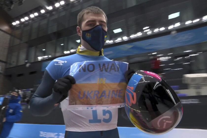 In this frame from video, Vladyslav Heraskevych, of Ukraine, holds a sign that reads "No War in Ukraine" after finishing a run at the men's skeleton competition at the 2022 Winter Olympics, Friday, Feb. 11, 2022, in the Yanqing district of Beijing. (NBC via AP)