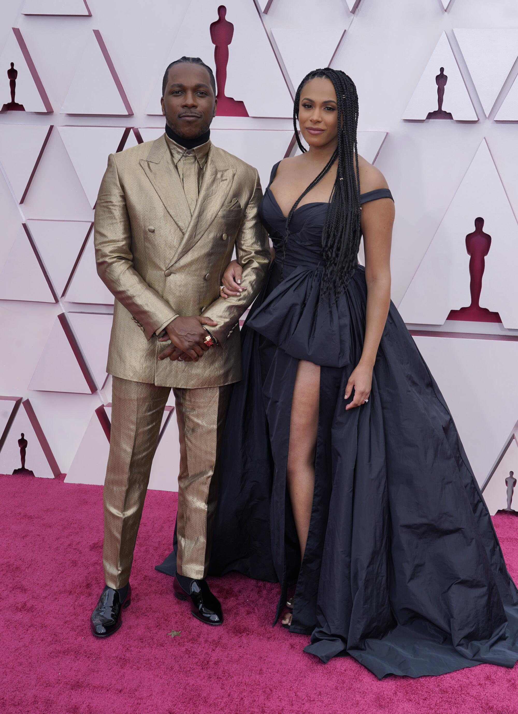 Leslie Odom Jr. in a gold suit and Nicolette Robinson in a dark low-cut dress with one leg showing. 