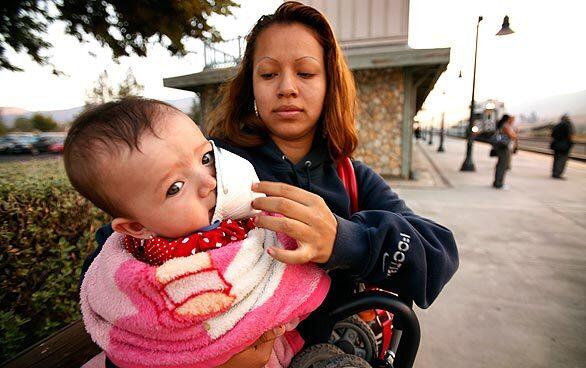 Jennifer DeLeon of Littlerock works to keep a mask on the face of her 8-month-old daughter, Emily Magana, as they prepare to board the 206 Metrolink Train at the Vincent Grade-Acton Station early Monday morning for a doctor's appointment in downtown Los Angeles. The mask was provided by a Metrolink supervisor.