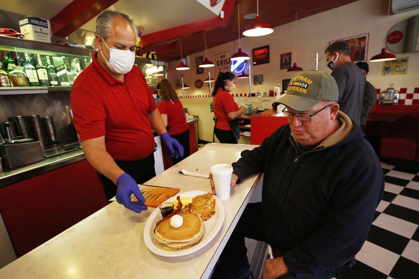 VENTURA, CA - MAY 21: Cal Youngblood, 75, is served breakfast by owner Raymundo Sanchez at Busy Bee Cafe on Main Street in downtown Ventura Thursday morning as Ventura County has become the largest county in Southern California to resume dine-in service at restaurants and in-store shopping joining a growing list of California counties that have been given permission to enter phase two of reopening after closures due to coronavirus Covid-19. Clay drove from Simi Valley to eat at Busy Bee Cafe for the first time in months as the restaurant holds special memories because his Mother worked there for many years in the 1960's. "I couldn't wait to come back." He said. Downtown on Thursday, May 21, 2020 in Ventura, CA. (Al Seib / Los Angeles Times)