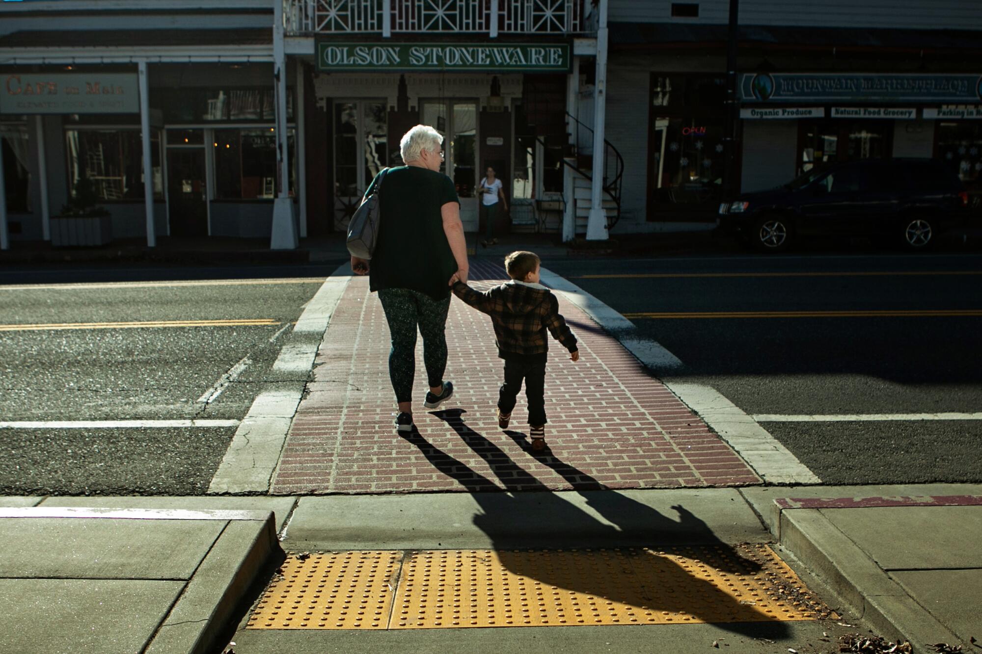 A woman holding the hand of a toddler crosses Main Street in Weaverville, Calif. 