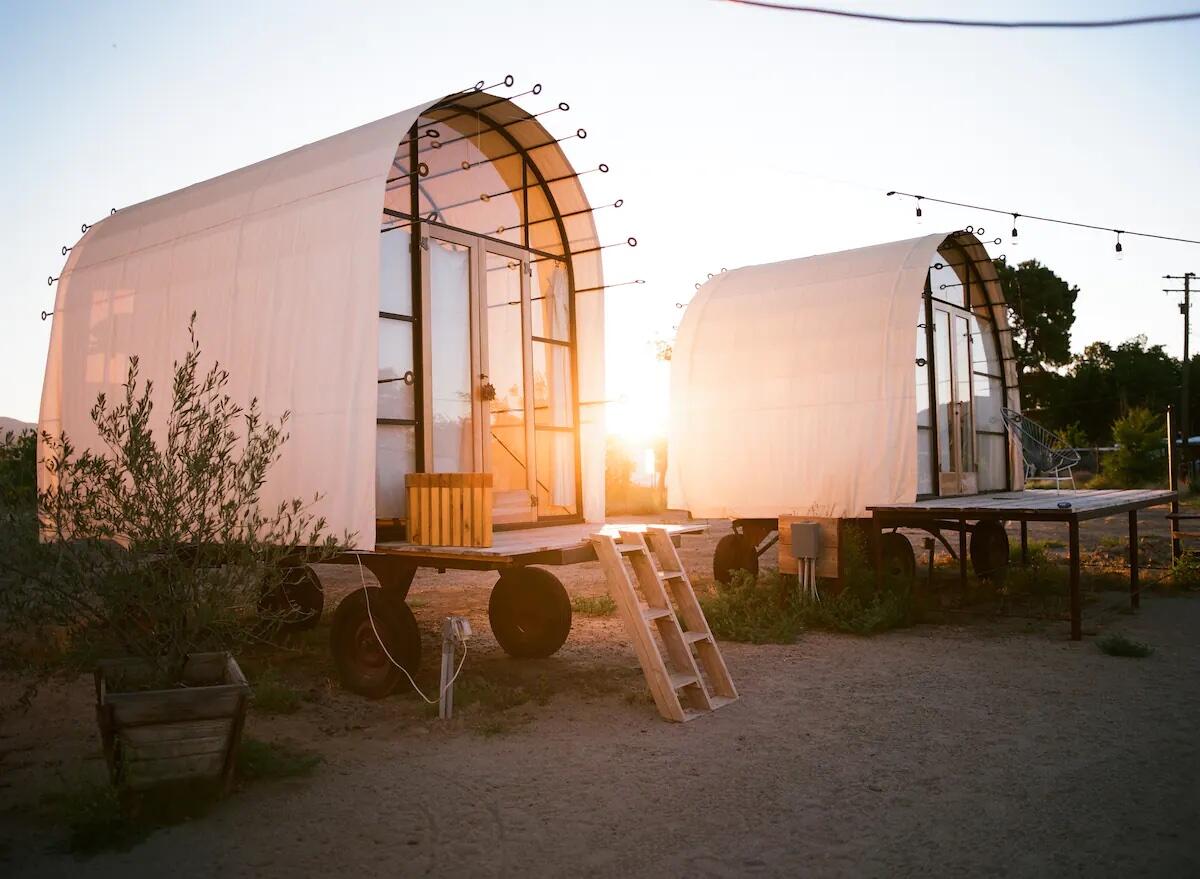 Two rounded-top glamping huts with the sun low behind them.