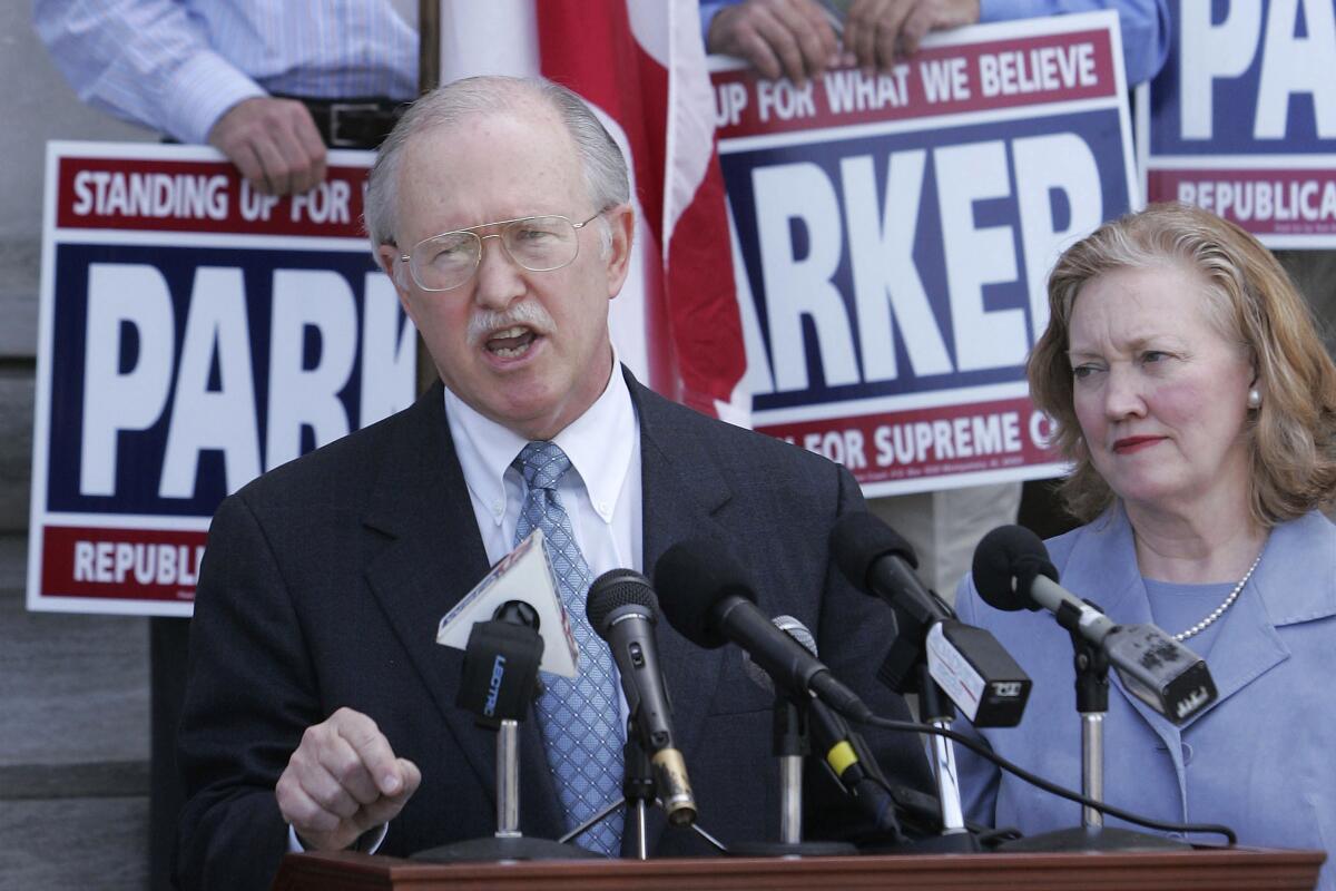 Alabama Supreme Court Chief Justice Tom Parker speaks at a lectern flanked by campaign signs.