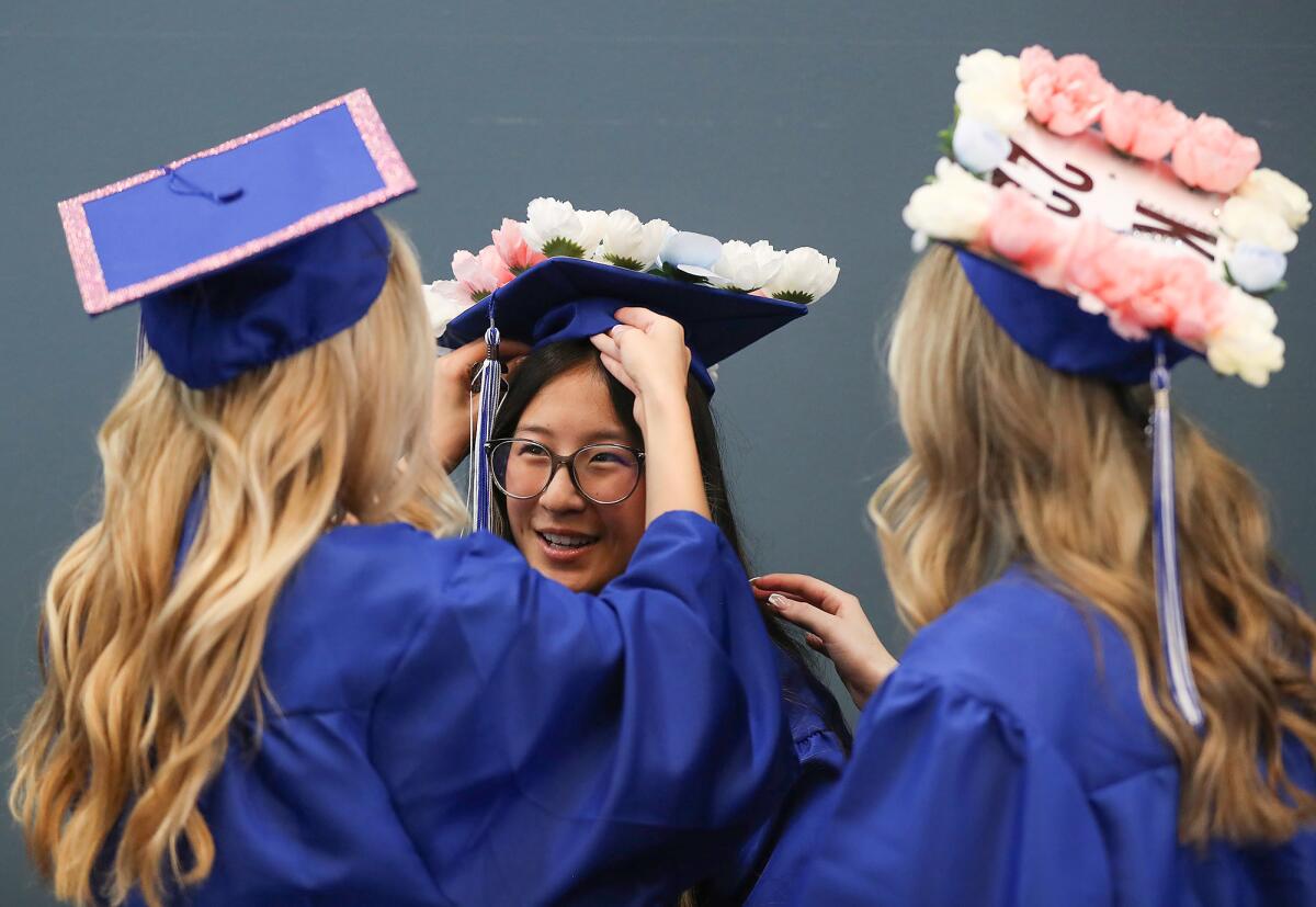 Graduate Evelyn Meek smiles as Kendal Ussery and Kaia Seck, from left, adjust her cap and gown.