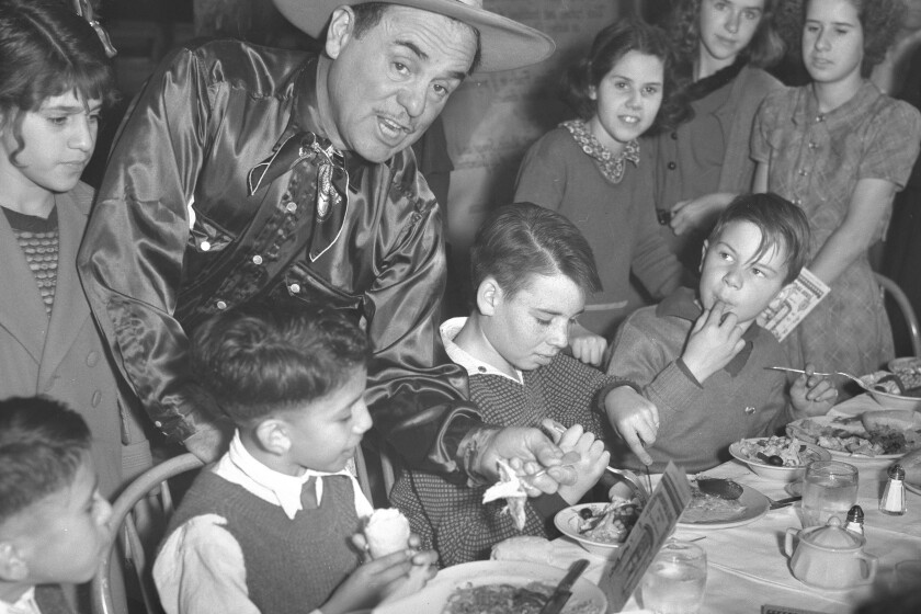 A man in a silk shirt and cowboy hat bands over to take a bite of turkey from a child's plate.