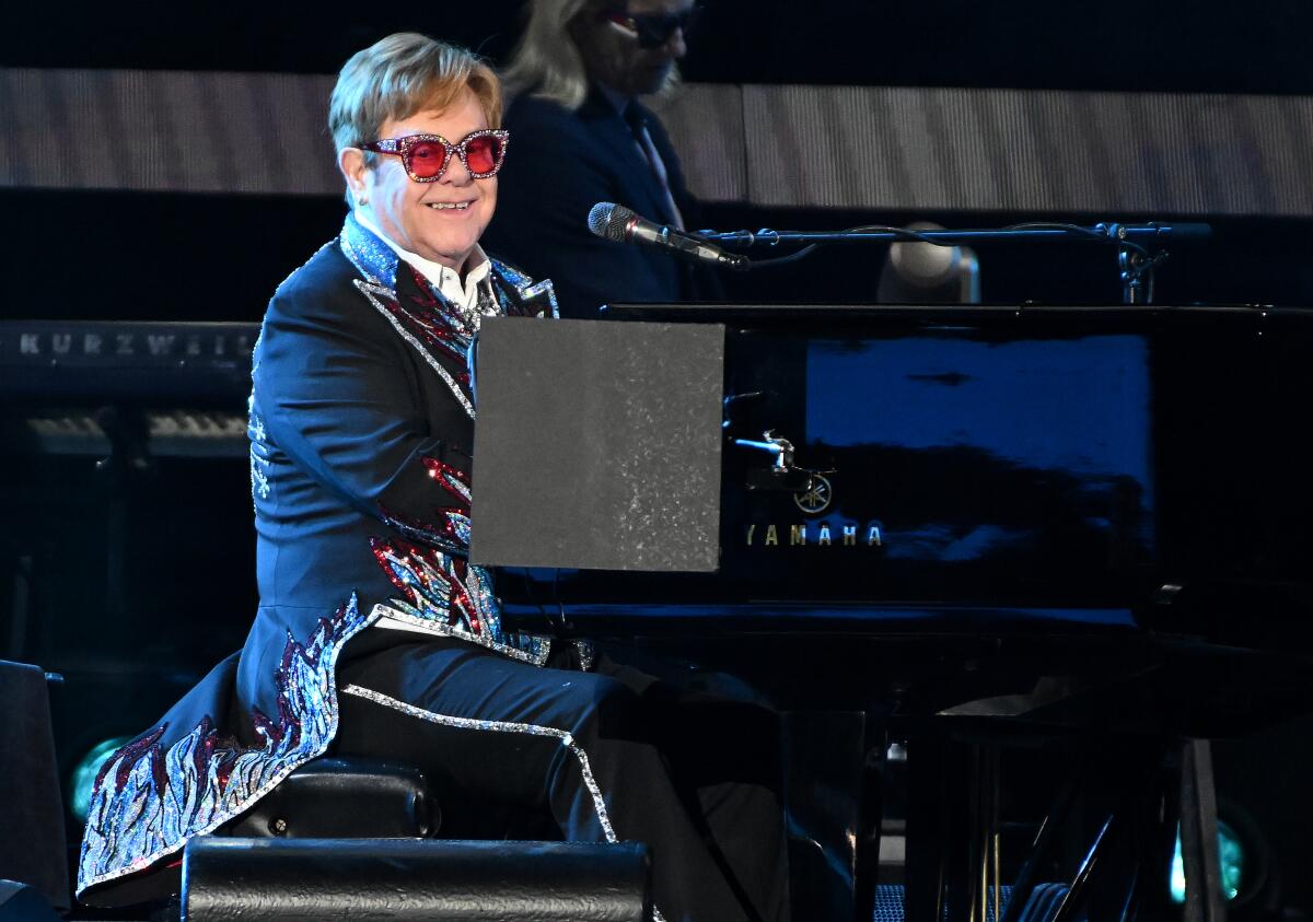 A musician wearing pink-tinted glasses sits behind a piano onstage.