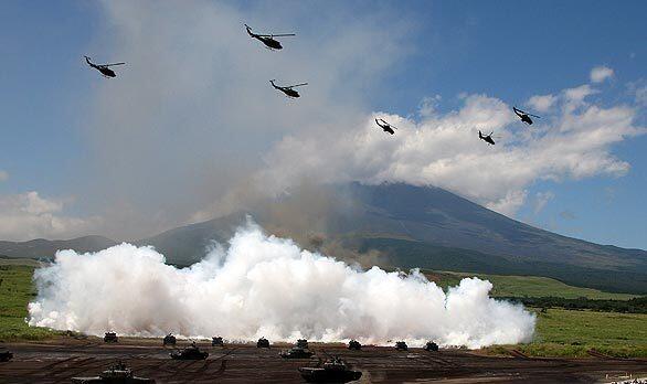 Tanks fire as helicopters fly above during an exercise by the Japan Ground Self-Defense Force at the foot of Mt. Fuji in Gotemba, Japan. About 2,400 personnel and 60 tanks and armed trucks participated in the drill.