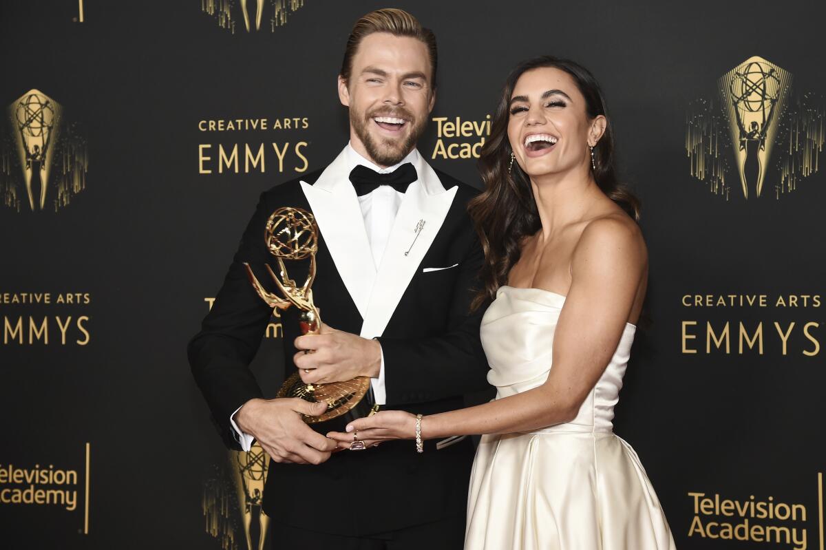 Derek Hough in a tuxedo and Hayley Erbert in a dress embrace and smile together while holding a gold statue Emmy award