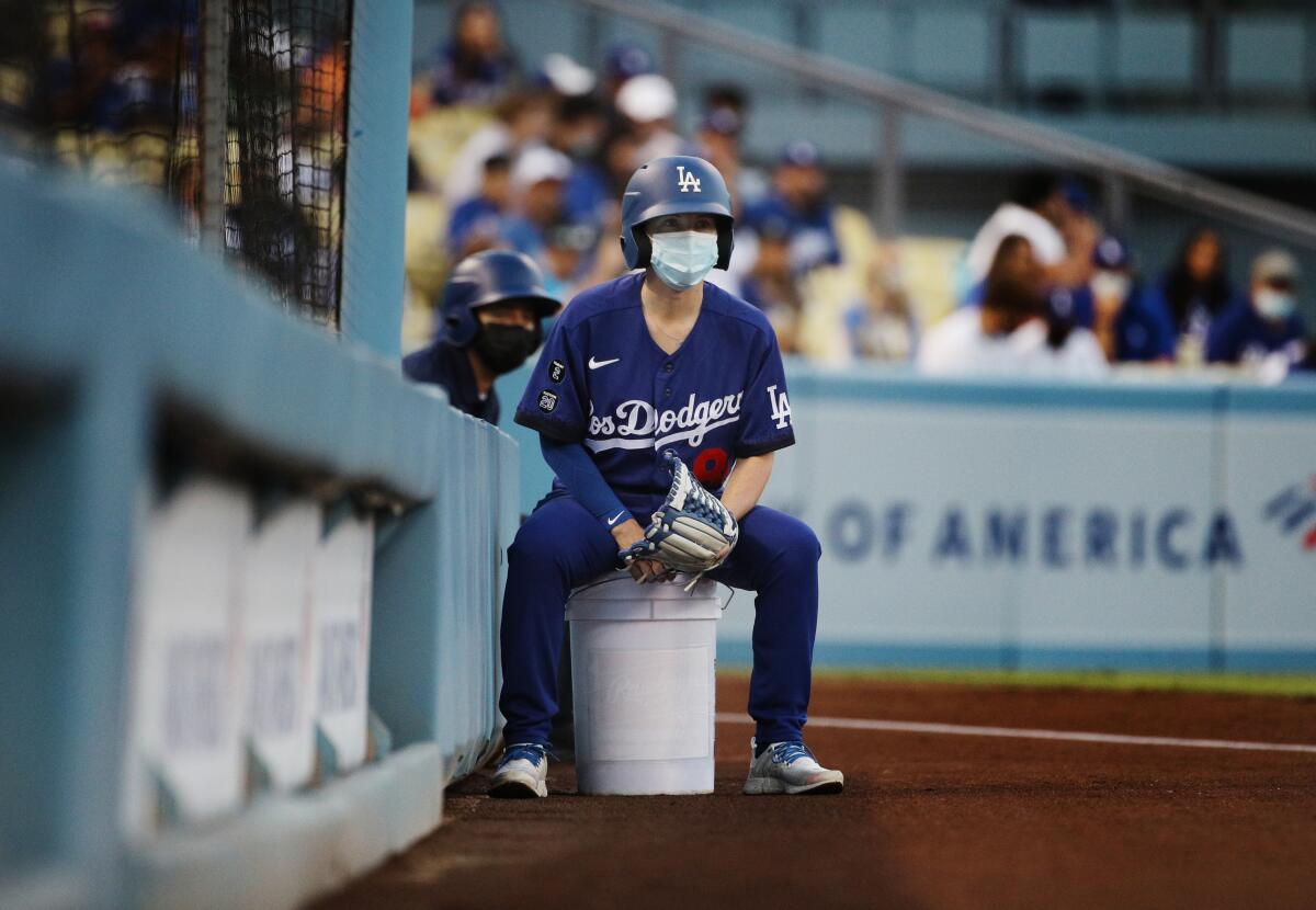The Los Angeles Dodgers ball girl sits on a bucket while wearing a mask.