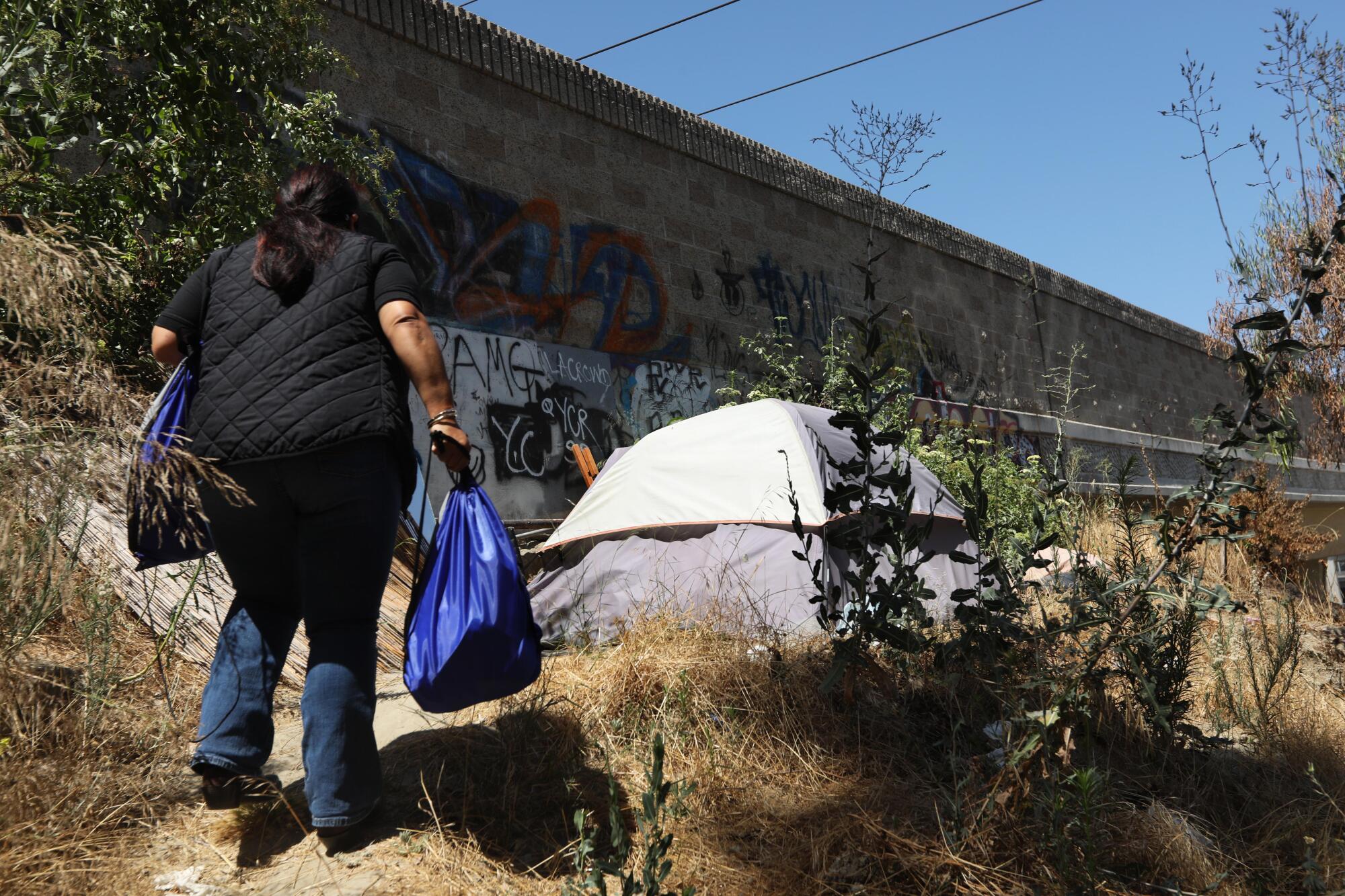 Outreach worker Kim Barnett takes food to a person along the 105 Freeway in Downey.