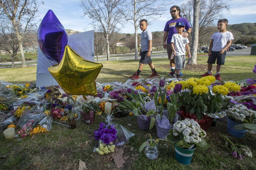 CALABASAS, CA-JANUARY 31, 2020: Ron Bio, 38, his nephew Branden Parry, left, son Gabriel, 9, middle, and nephew Dylan Parry, 8, right, visit a memorial at Juan Bautista de Anza Park in Calabasas for the 9 victims of a helicopter crash, that included Los Angeles Lakers legend Kobe Bryant and his 13 year old daughter, Gianna. (Mel Melcon/Los Angeles Times)