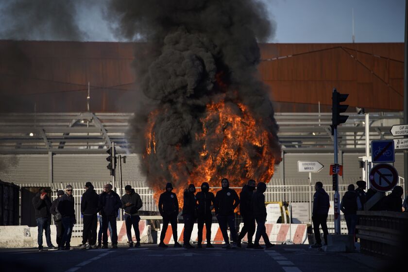 Dock workers stand in front of a burning barricade next the port of Marseille southern France, Wednesday, March 22, 2023.The bill pushed through by President Emmanuel Macron without lawmakers' approval still faces a review by the Constitutional Council before it can be signed into law. Meanwhile, oil shipments in the country were disrupted amid strikes at several refineries in western and southern France. (AP Photo/Daniel Cole)