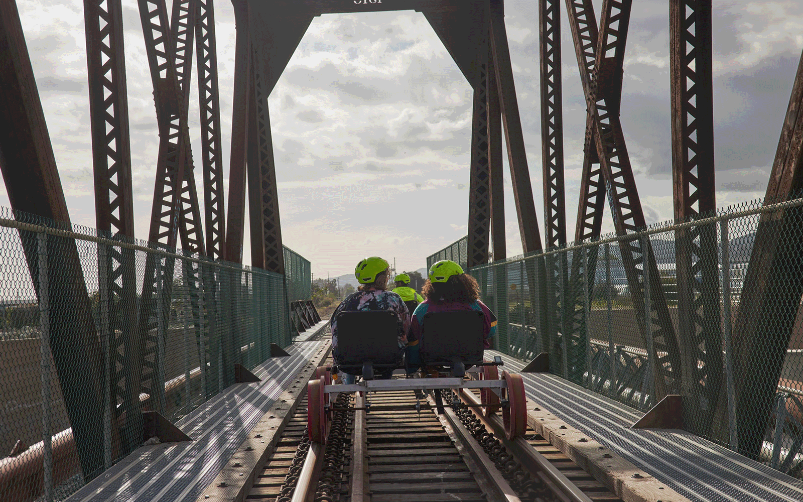 A gif of two people, viewed from behind, railbiking across a bridge.