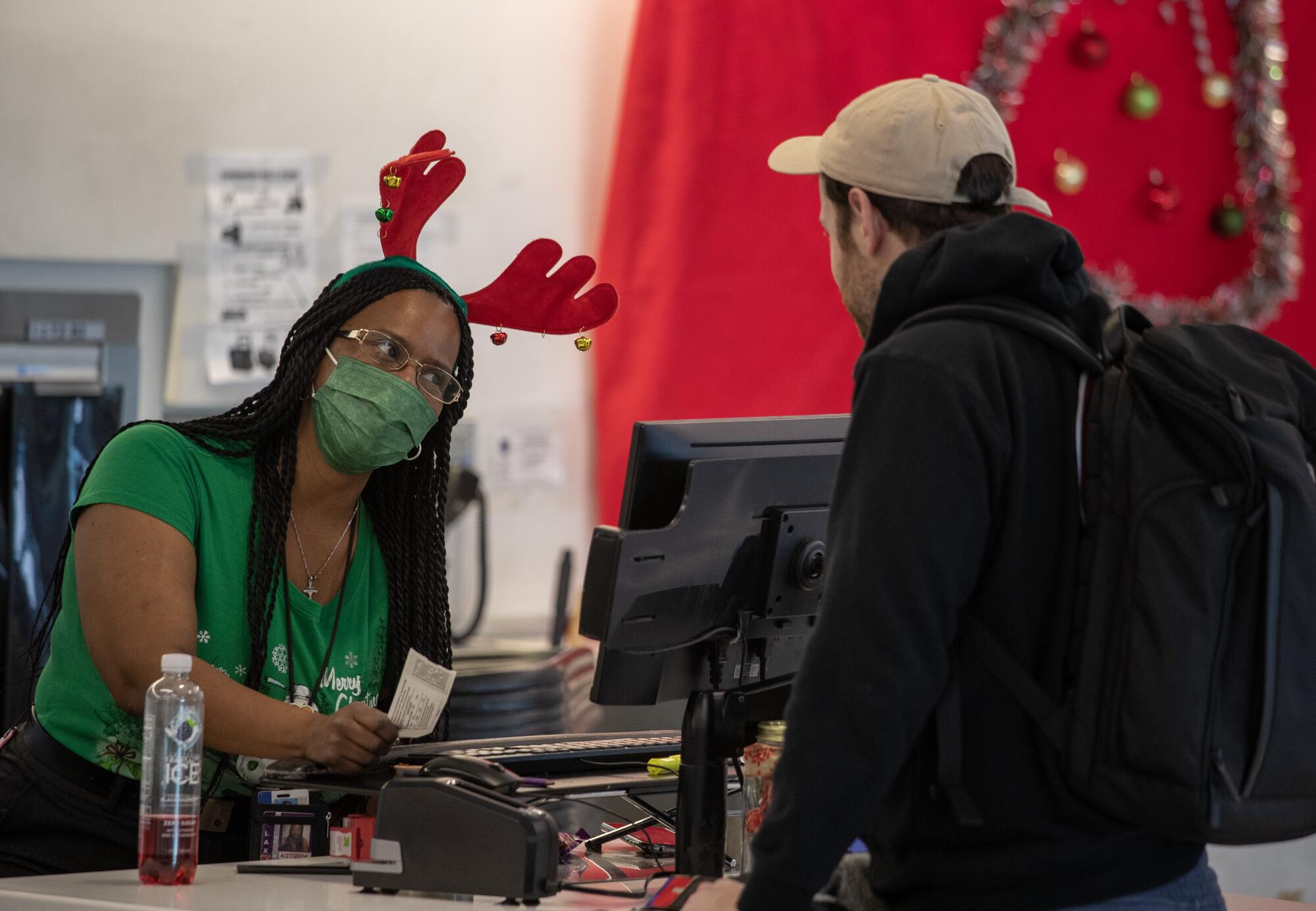 A woman wearing a green shirt and red antlers helps a holiday traveler.