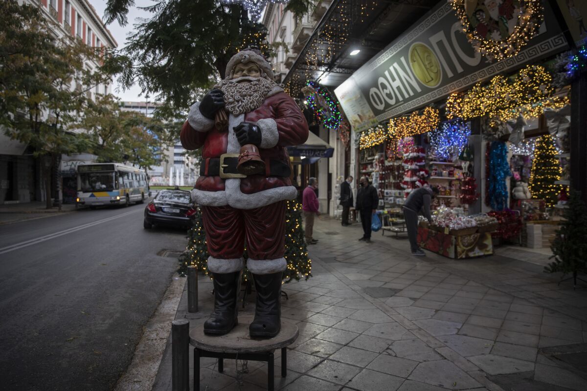 A Santa Claus stands outside a Christmas decoration shop, in central Athens, on Monday, Dec. 7, 2020. Despite a significant drop in cases over the past week, authorities have extended the countrywide lockdown to Dec. 14, but have allowed certain shops, including those selling Christmas-related merchandise, to open from Monday. (AP Photo/Petros Giannakouris)