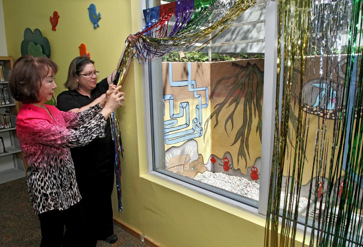 Montrose Library Supervisor Tiffany Barrios, right, holds open celebratory ribbons as Friends of the Glendale Public Library member Nini Maldonado takes a photo of a new mural created by Daily High School design class students, in Montrose on Tuesday, March 15, 2016.