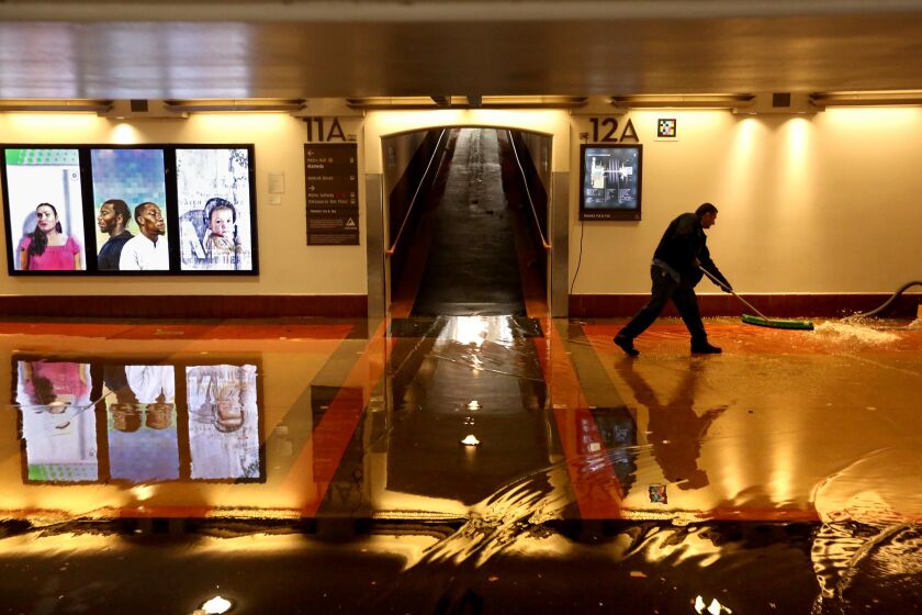 LOS ANGELES, CA - JANUARY 10, 2023 - - A Metro worker clears a flooded section of the pedestrian walkway leading to train platforms on the main level of Union Station in downtown Los Angeles on January 10, 2023. Many commuters were shuttled over the flooded section caused by the latest rain storm in Southern California. (Genaro Molina / Los Angeles Times)