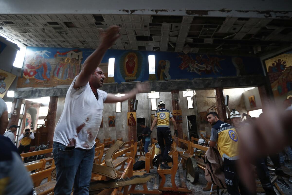 A man in a stained white T-shirt, arms outstretched, stands as people walk among pews in a church with images on the wall