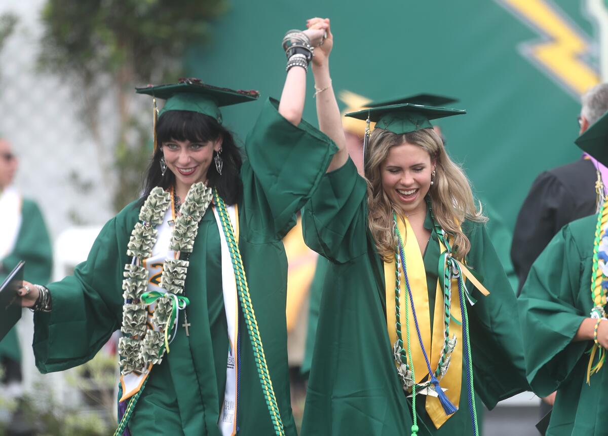 Two happy graduates raise their hands in joy after they both received their diplomas.