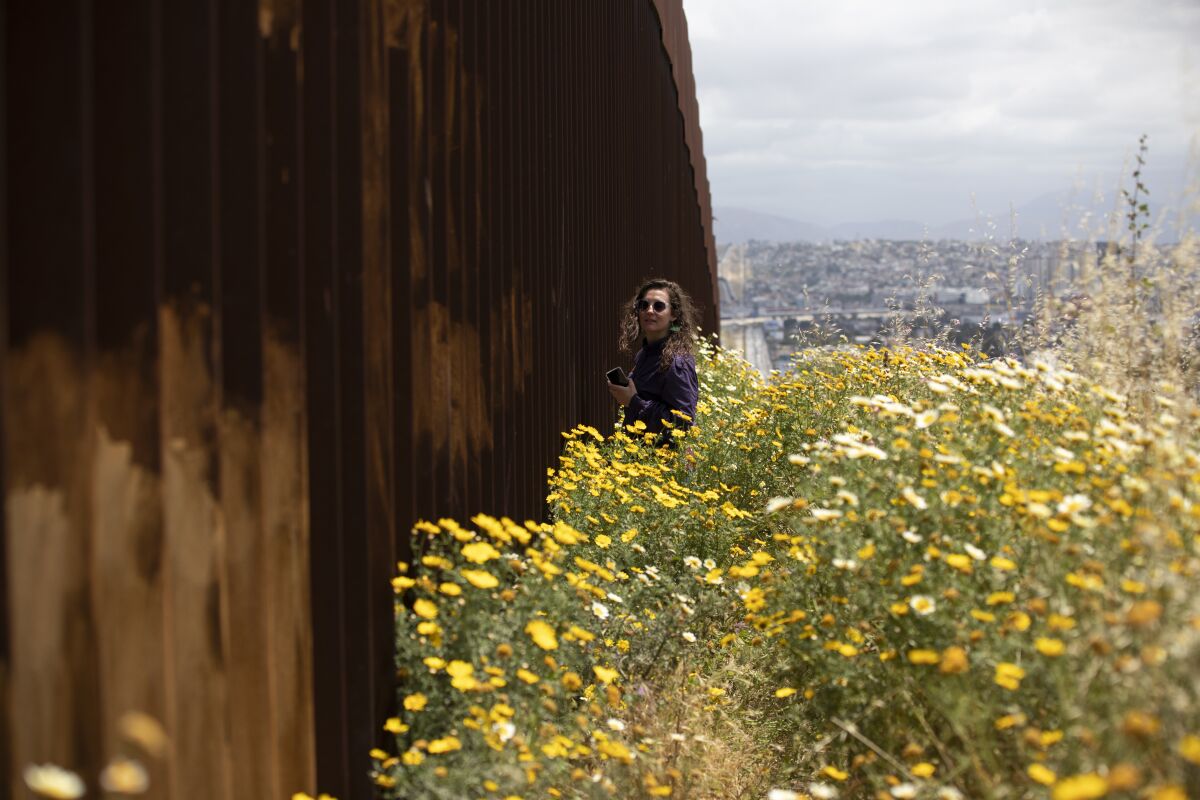 Reporter Kate Morrissey of the San Diego Union-Tribune stands next to the border wall on the Tijuana side