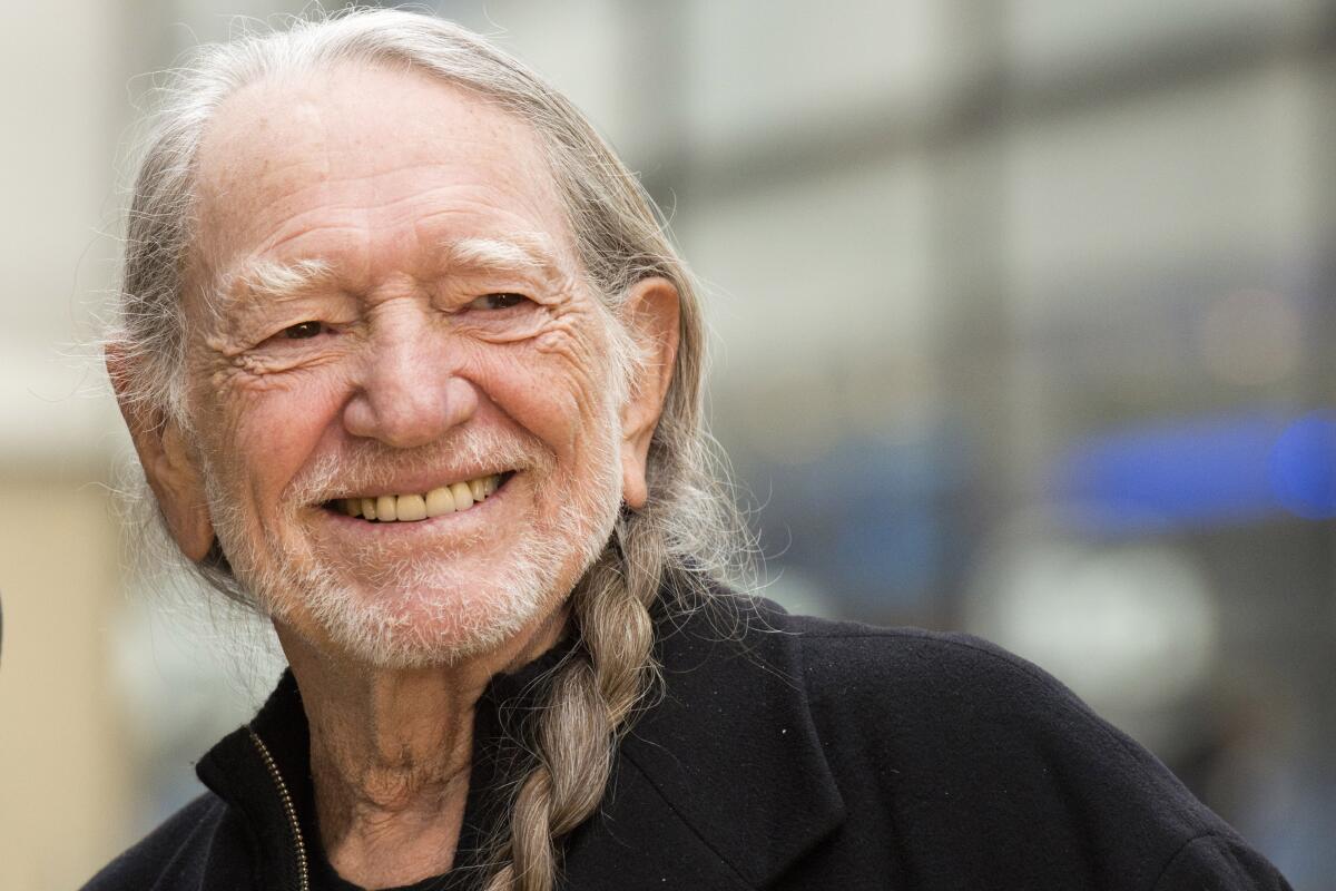 Willie Nelson, with a braid in his gray hair, smiles against an out-of-focus background