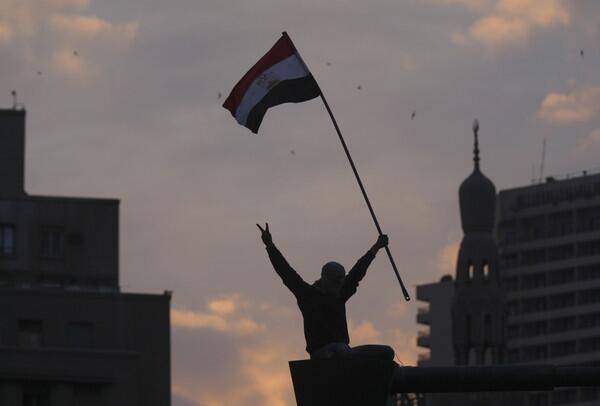 A protester waves an Egyptian flag after he climbed on a lampost during a demonstration in Tahrir square in downtown Cairo, Egypt, at dusk.
