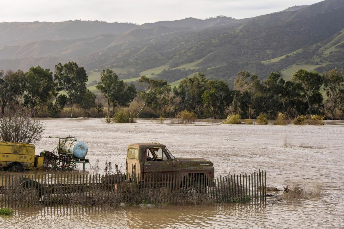 A truck is surrounded by floodwaters from the Salinas River. Trees and hills are in the background.
