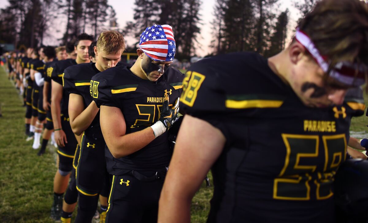 Lukas Hartley, second from right, bows his head with teammates during a moment of silence for the 86 victims of the Camp Fire.