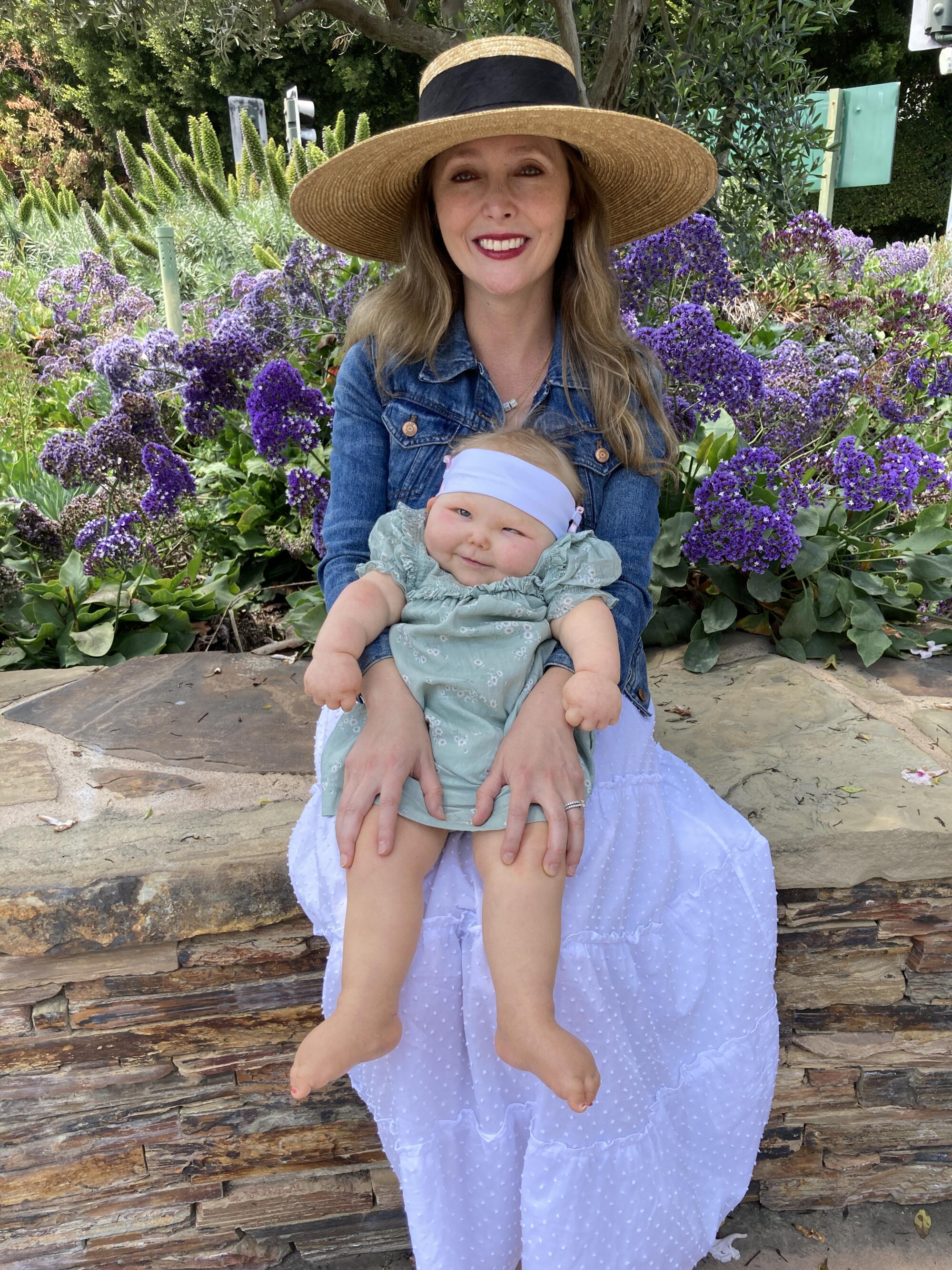 A woman sits on a stone wall holding a smiling baby on her lap.