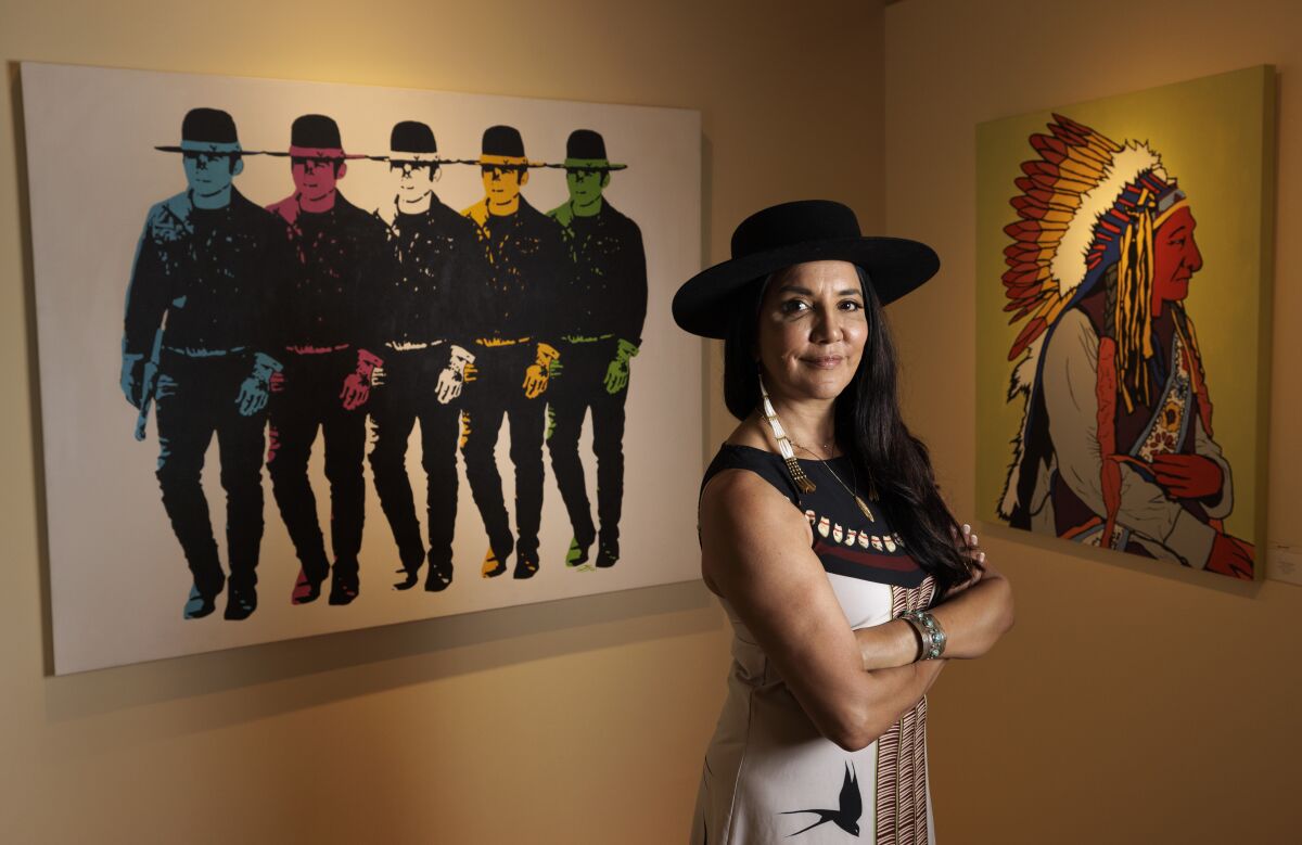 Indigenous entrepreneur Ruth-Ann Thorn stands next to paintings by Joe Hopkins, titled "Billy Jacks" and "Sitting Bull