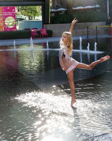 A young girl strikes a ballet pose in a fountain at a park