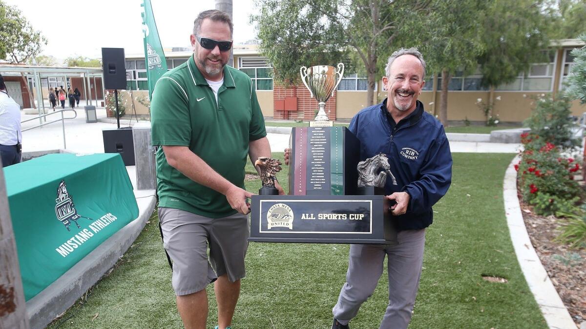 Costa Mesa athletic director Mike Ofer, left, and Newport Rib Company owner John Ursini carry the All-Sports Cup trophy to the celebratory luncheon at Costa Mesa High on Thursday.