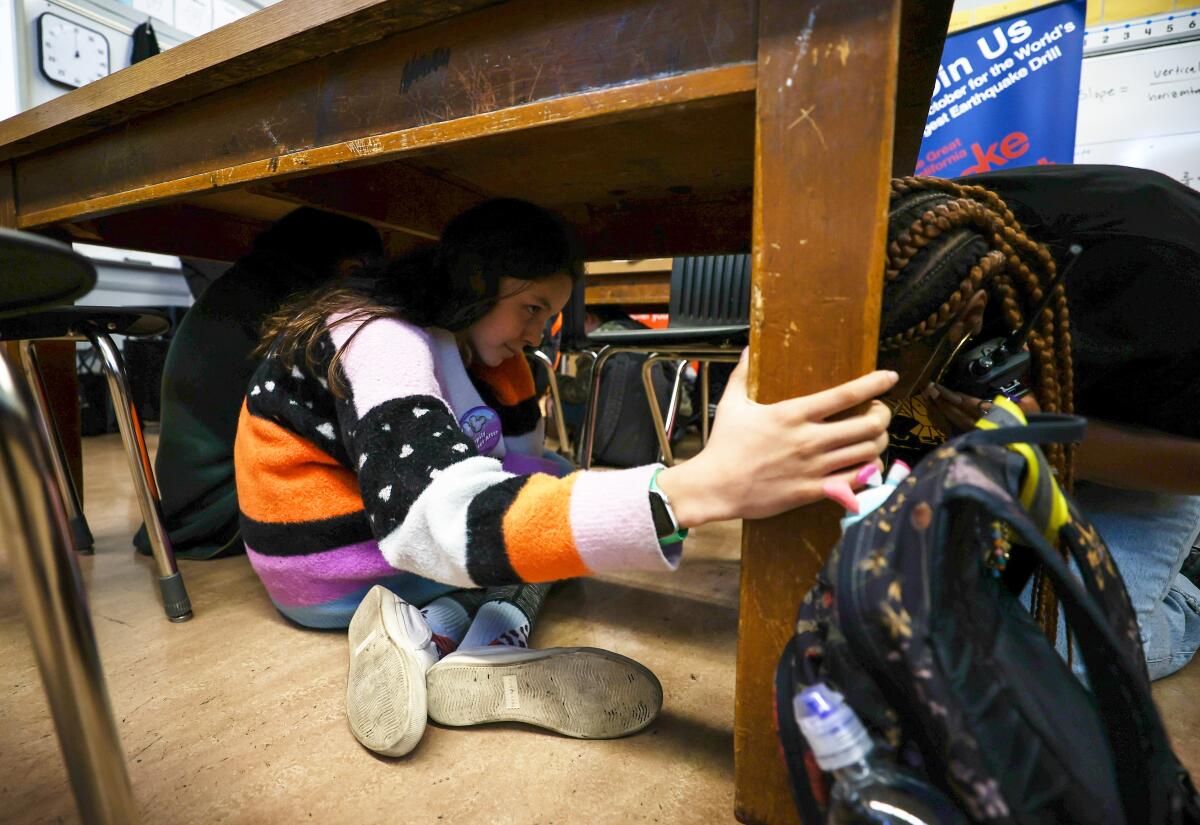 A student sits under a desk in the Great California ShakeOut earthquake drill.