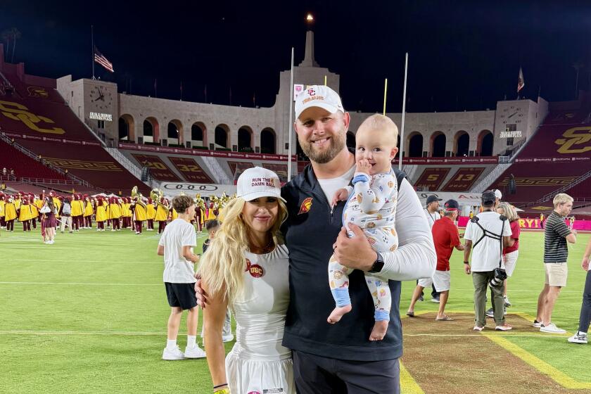 USC assistant coach Zach Hanson, his wife, Annie, and son Rock, pose for a photo on the field of the Coliseum.