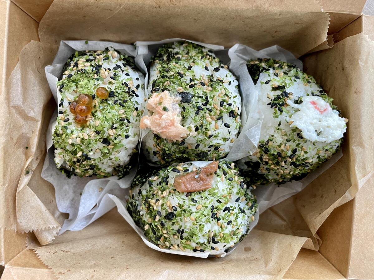 Rice balls with green and black speckles, wrapped in paper and nestled in a box