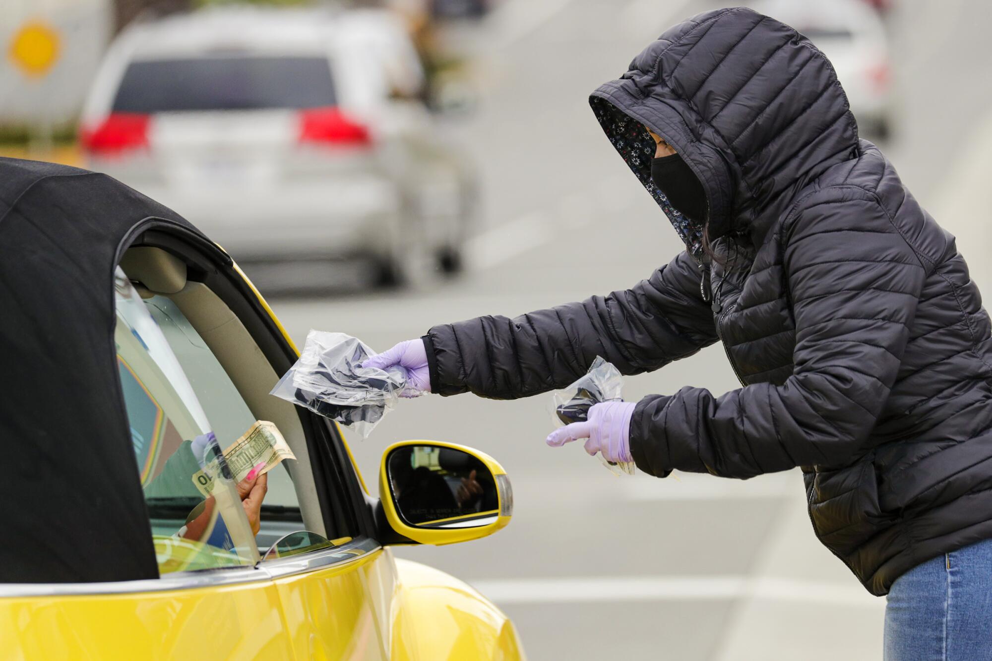 Stephanie Reyes, 16, sells masks to a traveler on the 3000 block of West Century Boulevard in Inglewood.