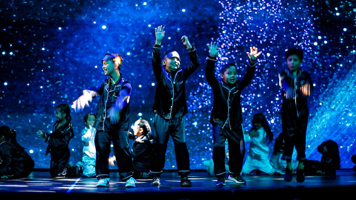 Niños en pijama negro bailan en el escenario frente a la noche estrellada.
