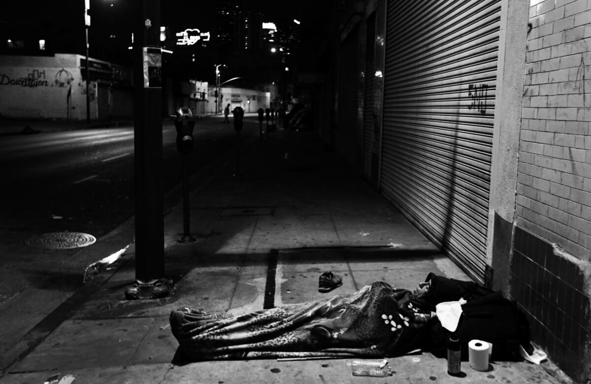 A man sleeps on the sidewalk beneath a blanket in downtown Los Angeles.