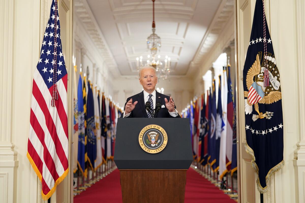 President Biden speaks from a lectern in front of a hallway lined with flags.