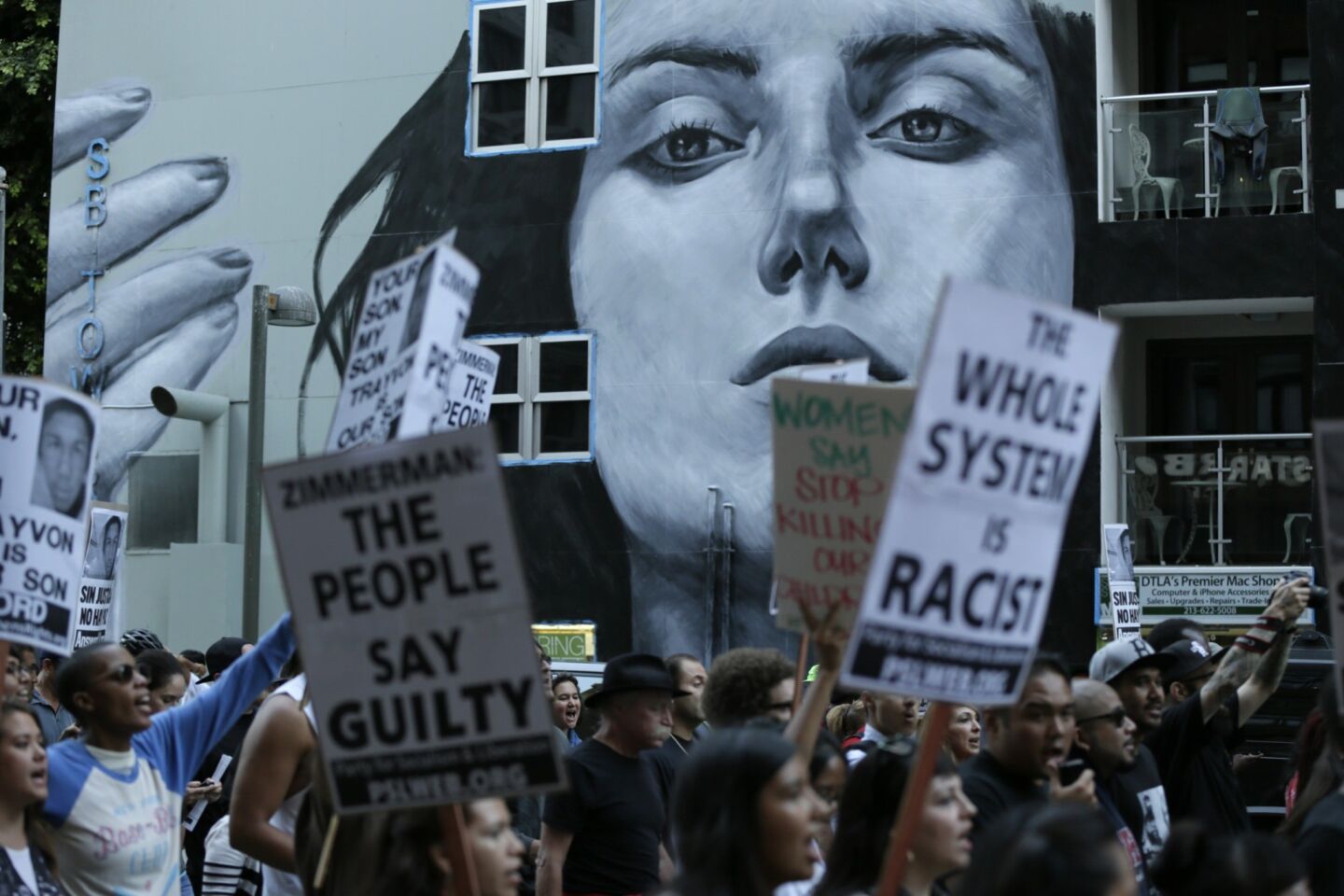Hundreds march along Spring Street in downtown Los Angeles protesting the not guilty-verdict of George Zimmerman for the murder of Trayvon Martin, holding signs that say "the whole system is racist."