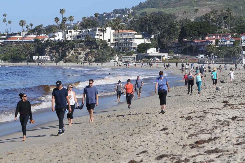 People walk the sands between Cleo St. and Main as Laguna Beach opened their beaches for recreation use between the hours of 6 to 10am on Tuesday. The beach will open for use Monday through Friday.